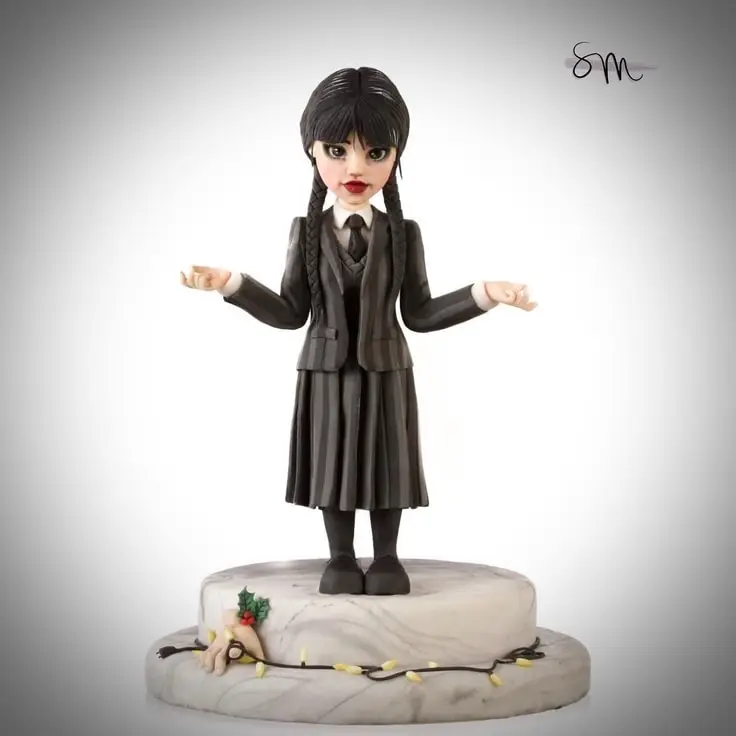 This cake topper features Wednesday Addams. The base of the topper has Thing setting out Christmas lights.