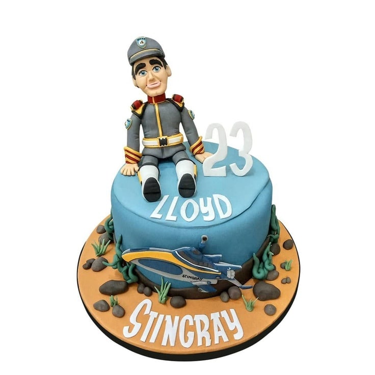 The cake and cake board look like the ocean floor which a 2-D Stringray is exploring. The cake is topped with a near perfect Troy Tempest figure.