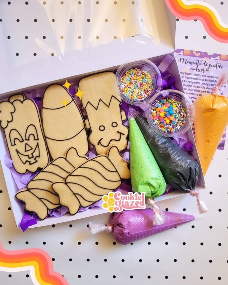 This cookies box contains cookies with black outlines, piping bags with icing and two containers of sprinkles.